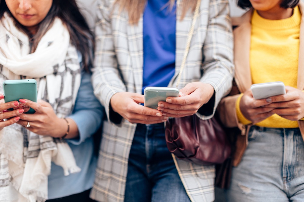 Las mujeres jóvenes que usan una aplicación de teléfono móvil al aire libre en la ciudad se centran en las manos centrales sosteniendo el teléfono inteligente